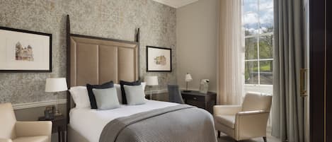 Habitación de hotel con una cama grande, dos mesitas de noche, una silla y un ventanal con cortinas.