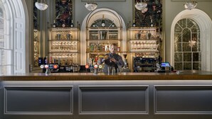 A bar area with a bartender, shelves of bottles, glasses, and a cash register. - Buxton Crescent (Buxton)