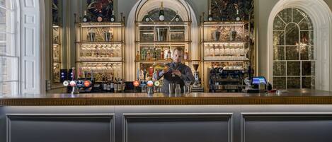A bar area with a bartender, shelves of bottles, glasses, and a cash register.