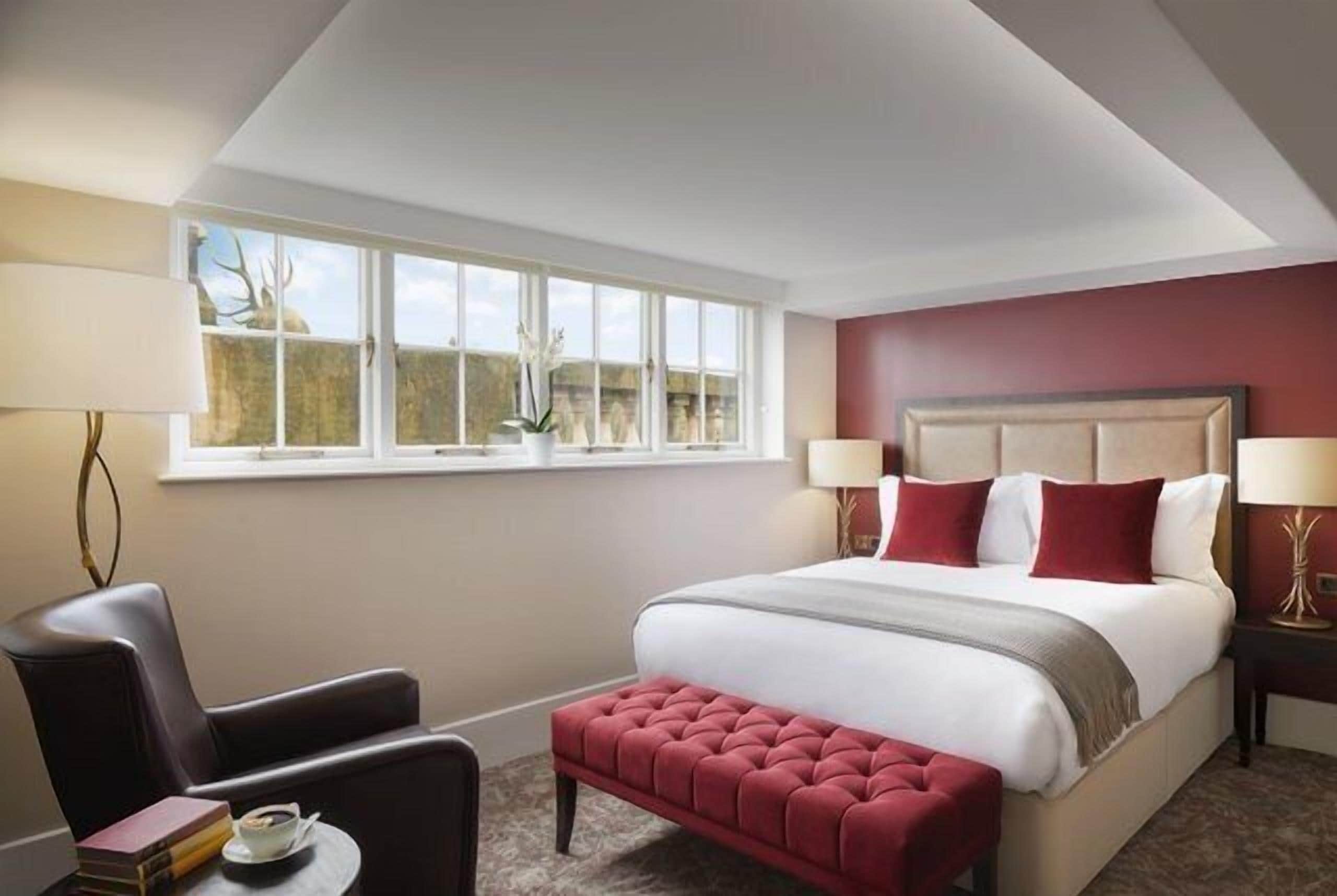 A bedroom with a large bed, a chair, a small table, and a window with a view.