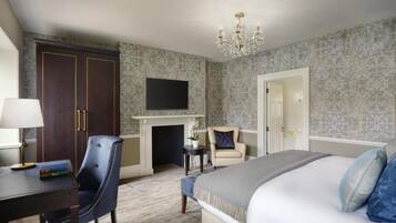 A hotel room with a bed, a desk with a lamp, a chair, a fireplace, and a TV on the wall.