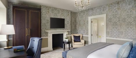 A hotel room with a bed, a desk with a lamp, a chair, a fireplace, and a TV on the wall.