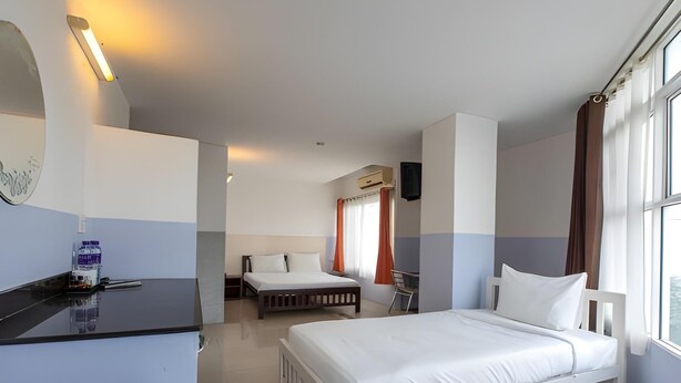 A hotel room with a bed, a desk, and a chair. There is a window with curtains, and an air conditioning unit on the wall.