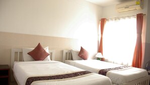 A hotel room with two beds, a nightstand, an air conditioning unit, and a window with curtains.