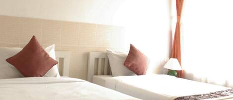 A hotel room with two beds, a nightstand, a lamp, and a window with curtains.