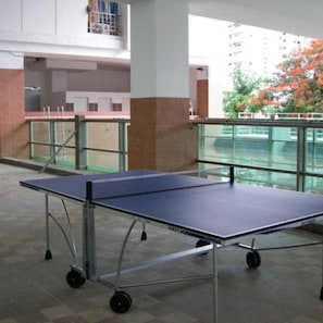 A ping pong table in a spacious indoor area with a glass railing and a view of a building outside. - Ratchada 17 Place (Bangkok)