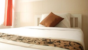 A hotel room with a bed, a white headboard, a brown pillow, and a patterned throw.