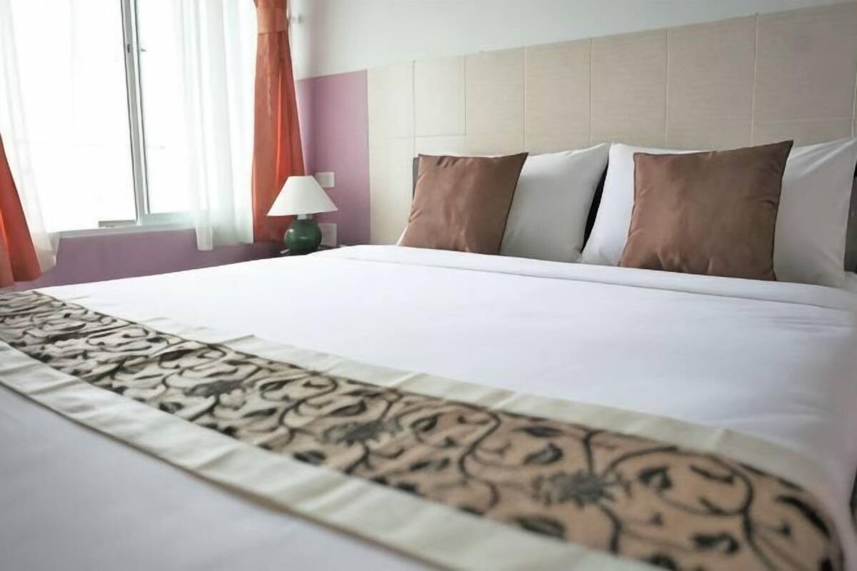 A hotel room with a large bed, a headboard, and a window with curtains.