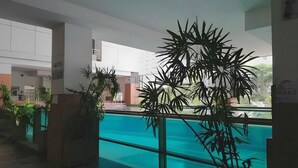 A modern indoor pool area with clear glass walls, potted plants, and a view of the outside. - Ratchada 17 Place (Bangkok)