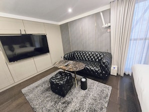 A living room with a TV, leather sofa, ottoman, and a coffee table. - The May Hotel (Seoul)