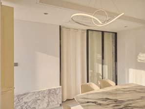 A modern dining area with a marble table, two chairs, and a contemporary light fixture.