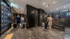 A modern hotel lobby with a reception desk, marble flooring, and a geometric patterned wall. - The May Hotel (Seoul)