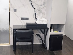 A room with a marble wall, a desk with a printer, a chair, a small cabinet, and a power outlet. - The May Hotel (Seoul)