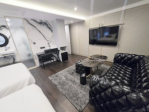 A modern living room with a black leather sofa, a white couch, a marble-patterned wall, a TV, and a small dining area. - The May Hotel (Seoul)
