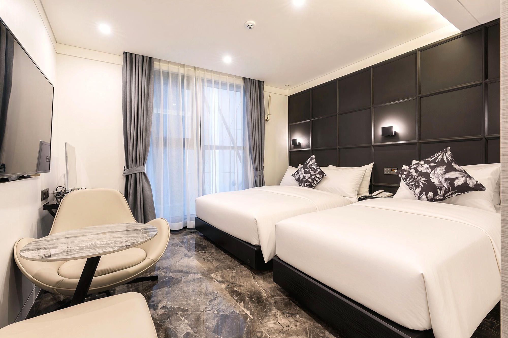 Une chambre d’hôtel avec deux lits, un bureau, une chaise, une télévision et une fenêtre avec des rideaux.