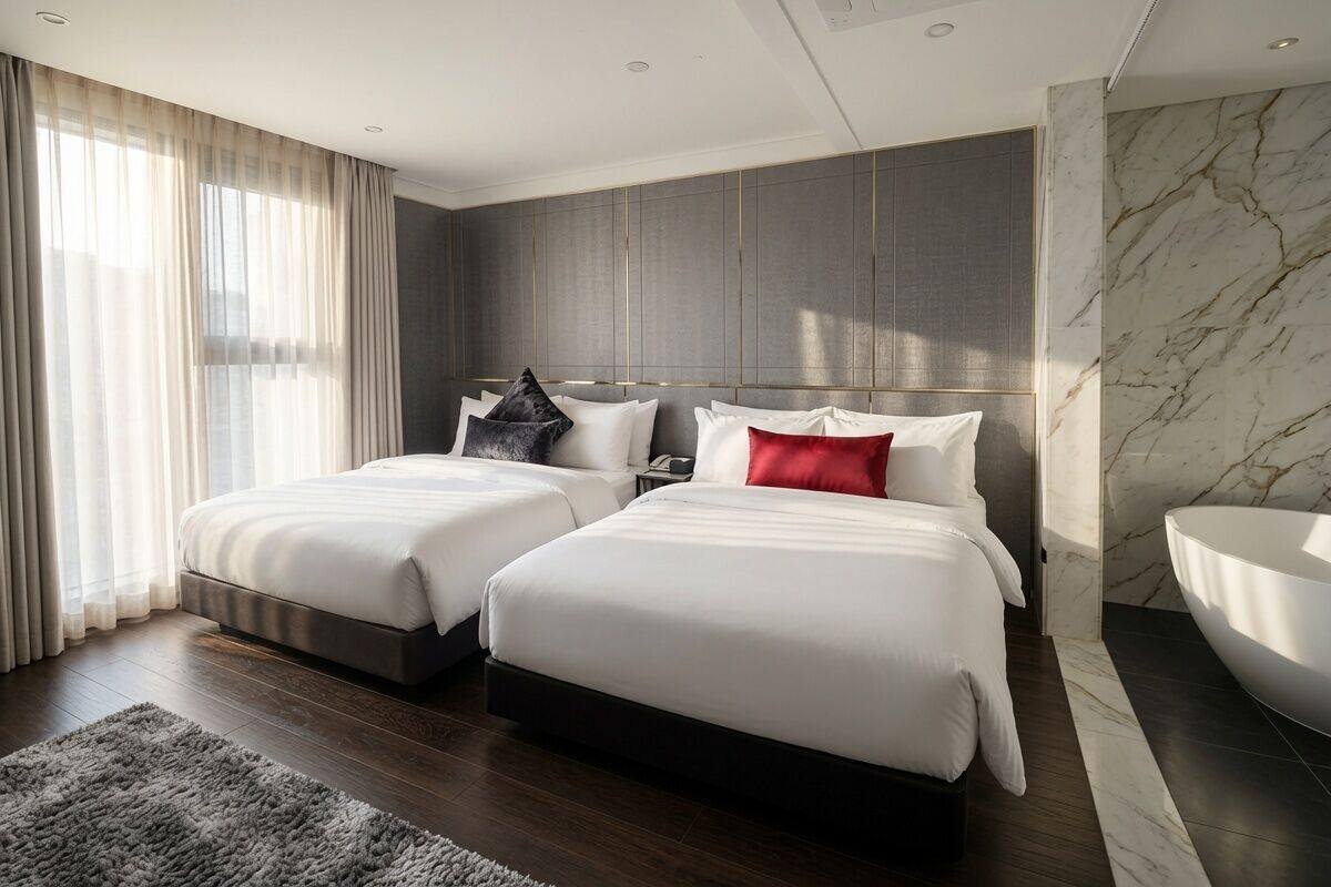 A modern hotel room with two beds, a large window with curtains, a marble wall, and a large white bathtub.