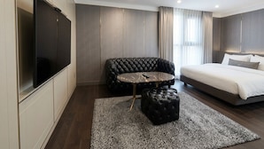 A modern hotel room with a bed, a seating area with a round table, and a large flat-screen TV. - The May Hotel (Seoul)