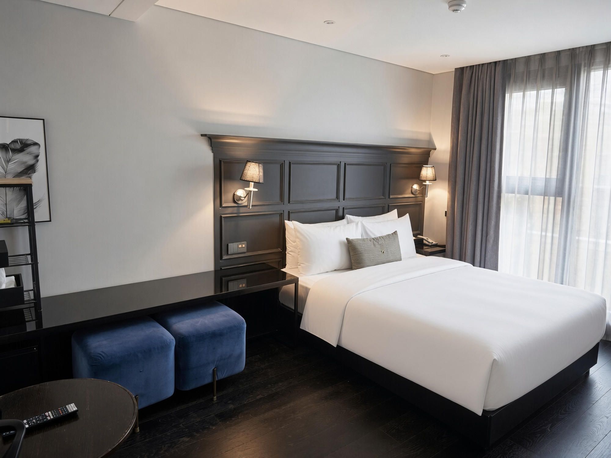 A hotel room with a large bed, bedside lamps, a desk with a chair, and a view of the outdoors through the window.