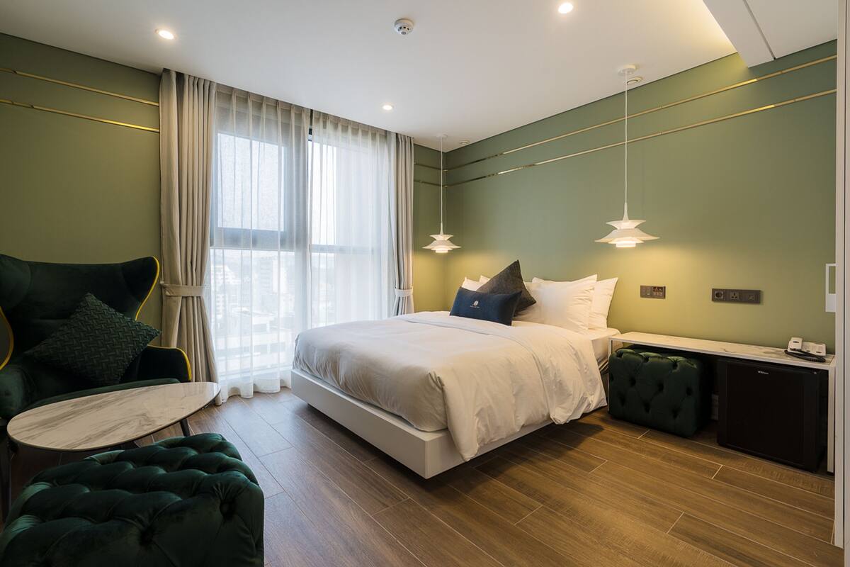 A modern bedroom with a bed, a green armchair, a small table, and a desk with a computer.