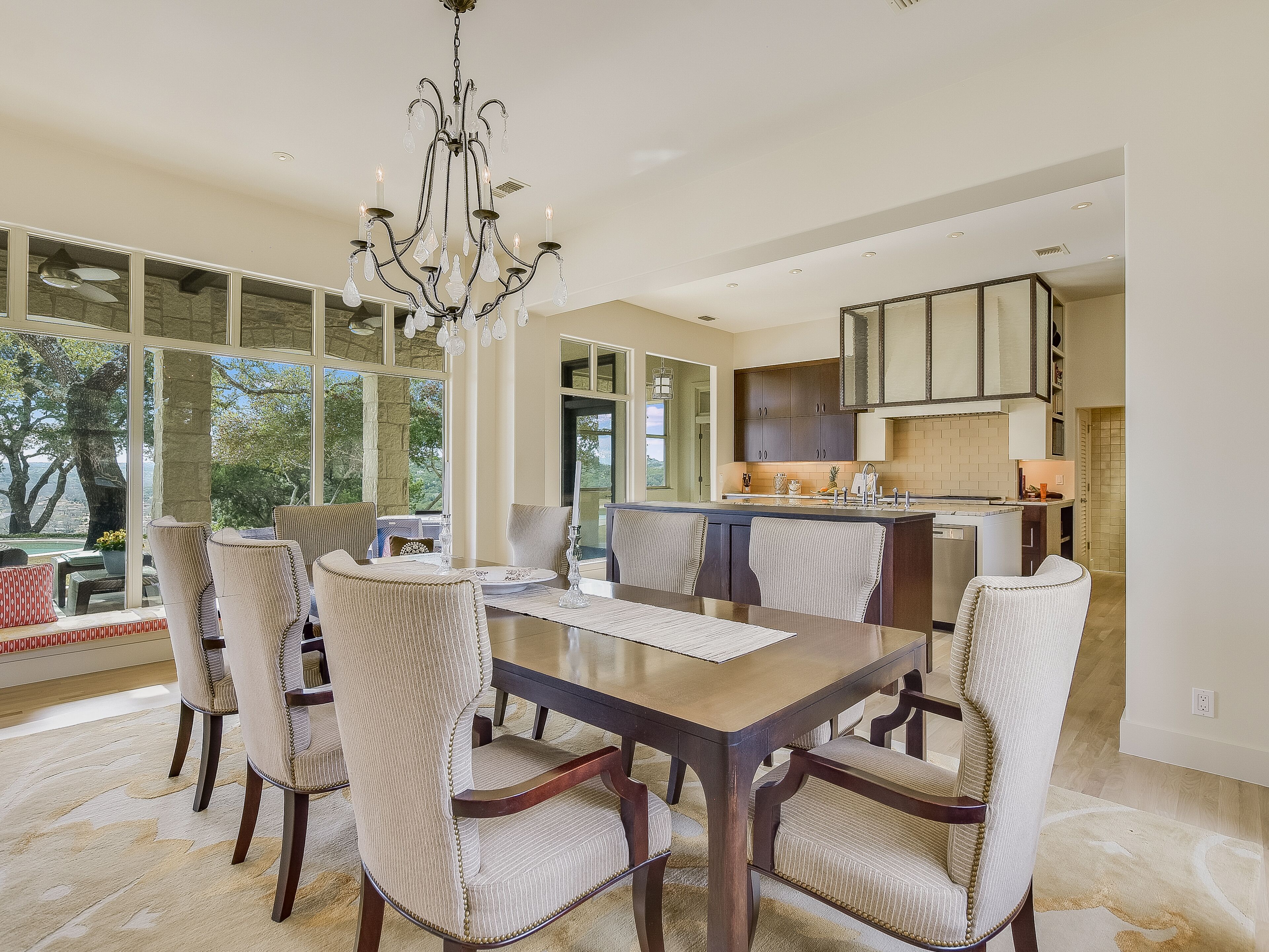 A spacious dining area with a large table and six chairs, a chandelier, and a view of the outdoors.