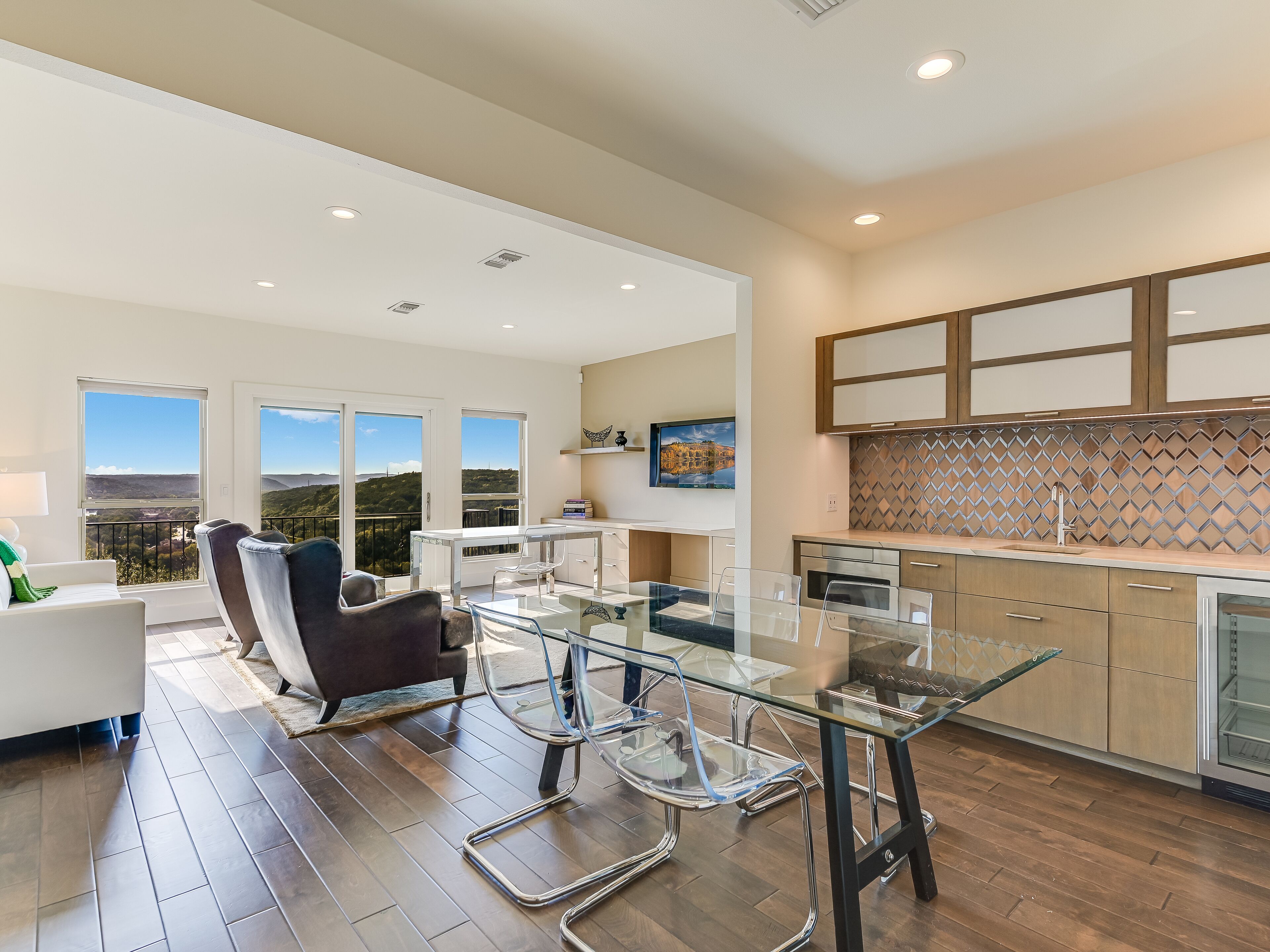 A modern kitchen with a glass dining table, stainless steel appliances, and a view of the outdoors.