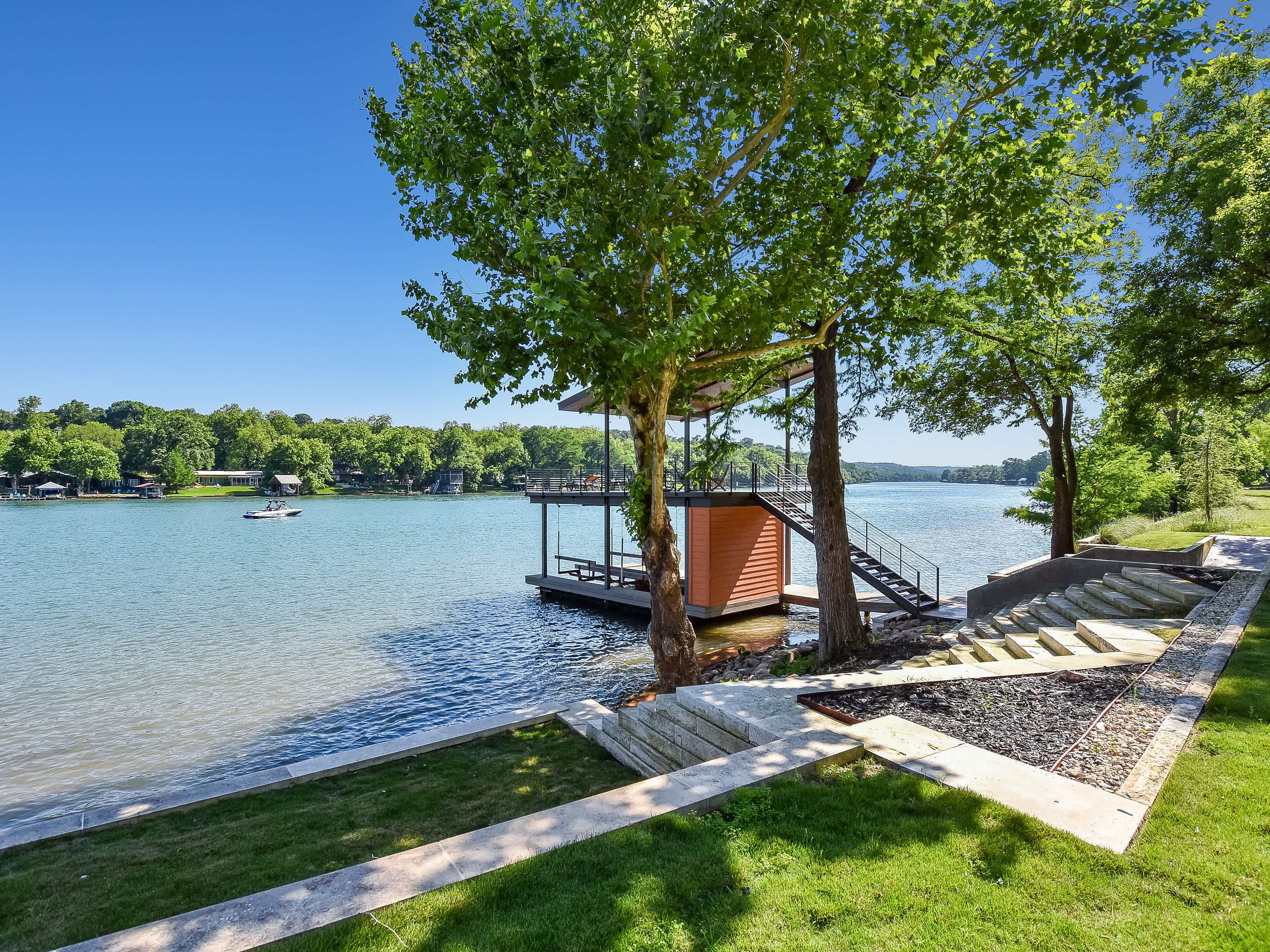 Une terrasse au bord du lac, dotée d’une structure en bois, d’un quai pour bateaux et d’une zone herbeuse avec des marches menant à un autre quai.