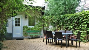 Un patio con una mesa y sillas, un banco y una puerta rodeada de follaje.