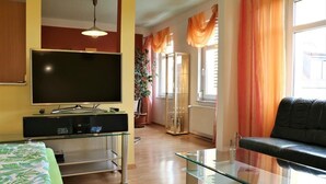 Una sala moderna con una televisión de pantalla plana, una mesa de centro de vidrio, un sofá negro y una cama con colcha verde y blanca.