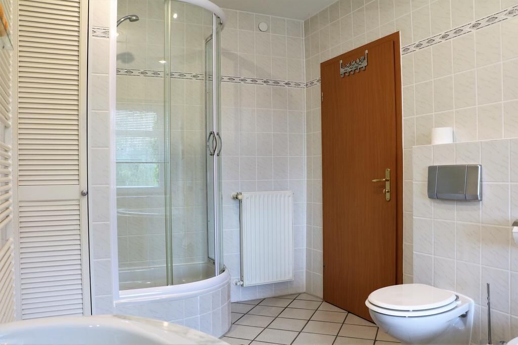 A bathroom with a glass shower enclosure, a white bathtub, a wooden door, and a toilet.