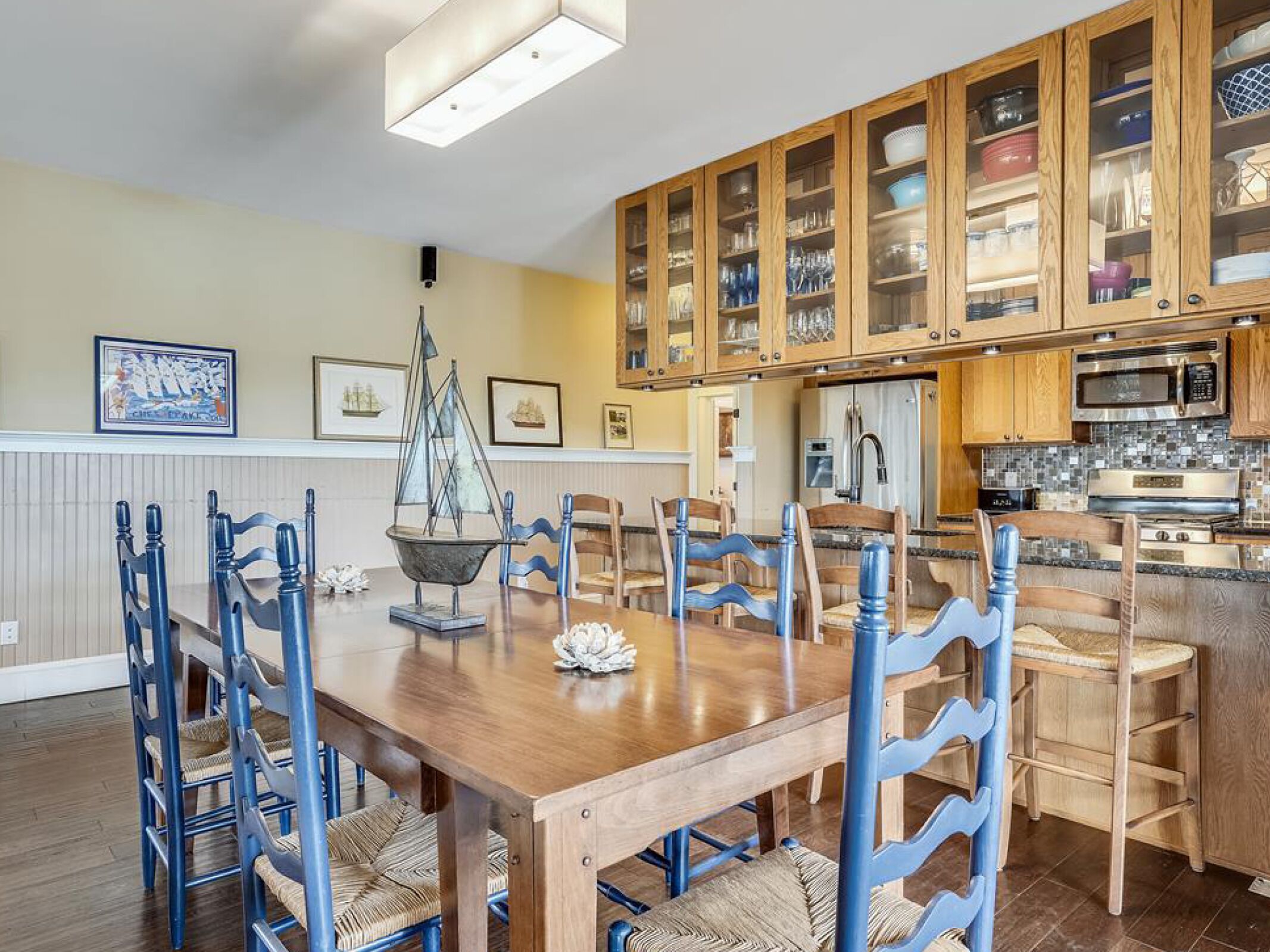 A dining area with a wooden table and blue chairs, a ship model, and framed pictures on the wall.