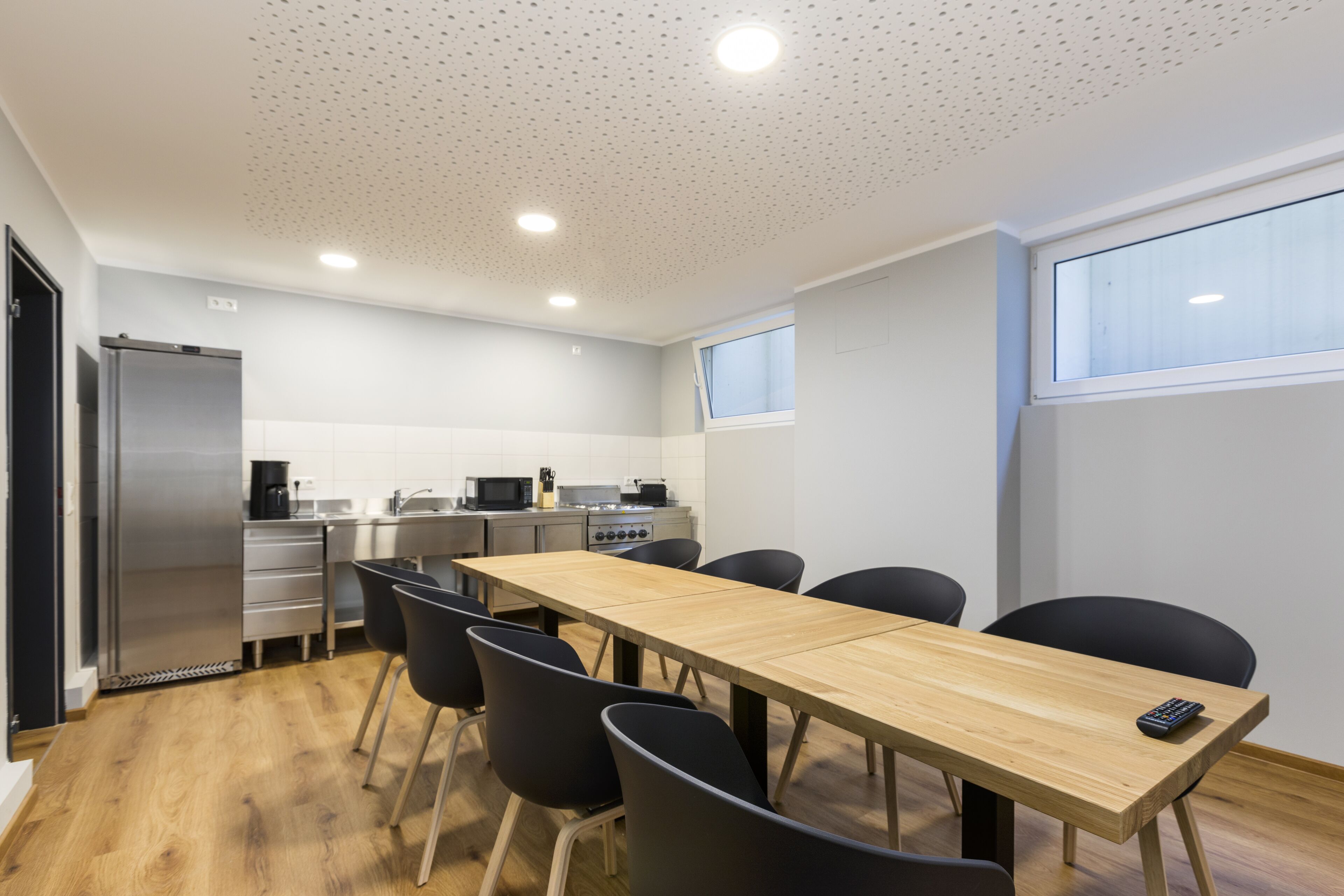 A modern kitchen with a wooden table and black chairs, a refrigerator, and a microwave.