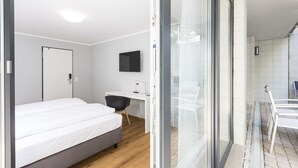 A modern hotel room with a bed, desk, and a view through a glass door. - mk | monteurzimmer eschborn (Eschborn)