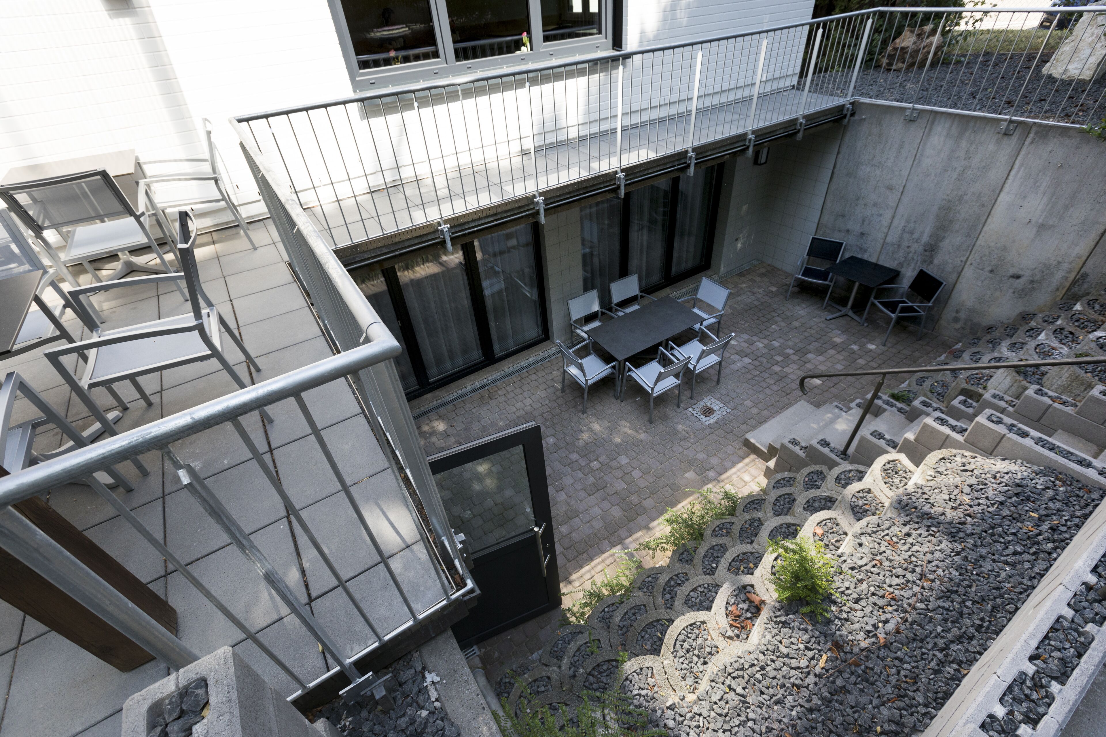 Eine Außenpatio-Terrasse mit Esstisch und Stühlen, ein kleiner Garten mit dekorativem Stegmuster und eine Betonmauer.