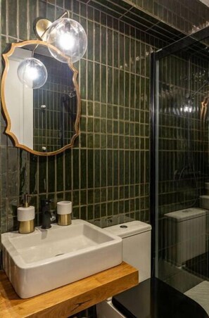 A bathroom with a white sink, two gold faucets, a wooden countertop, a mirror with a gold frame, and a shower area with a glass door.