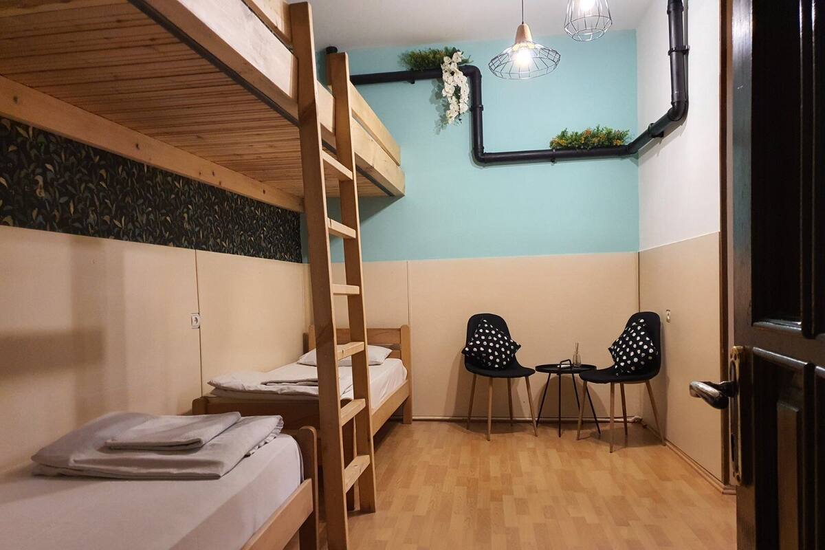 A bunk bed room with a wooden ladder, two chairs, and a small table.