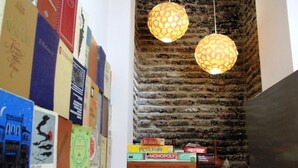 A room with a brick wall, a bookshelf with various books, and two hanging lamps. - Envoy Hostel (Tbilisi)