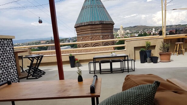 A rooftop terrace with a view of a historic building, a table with chairs, and potted plants. - Envoy Hostel (Tbilisi)