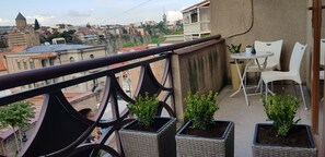 Un balcone con fioriere in vimini, un tavolo e sedie bianche.