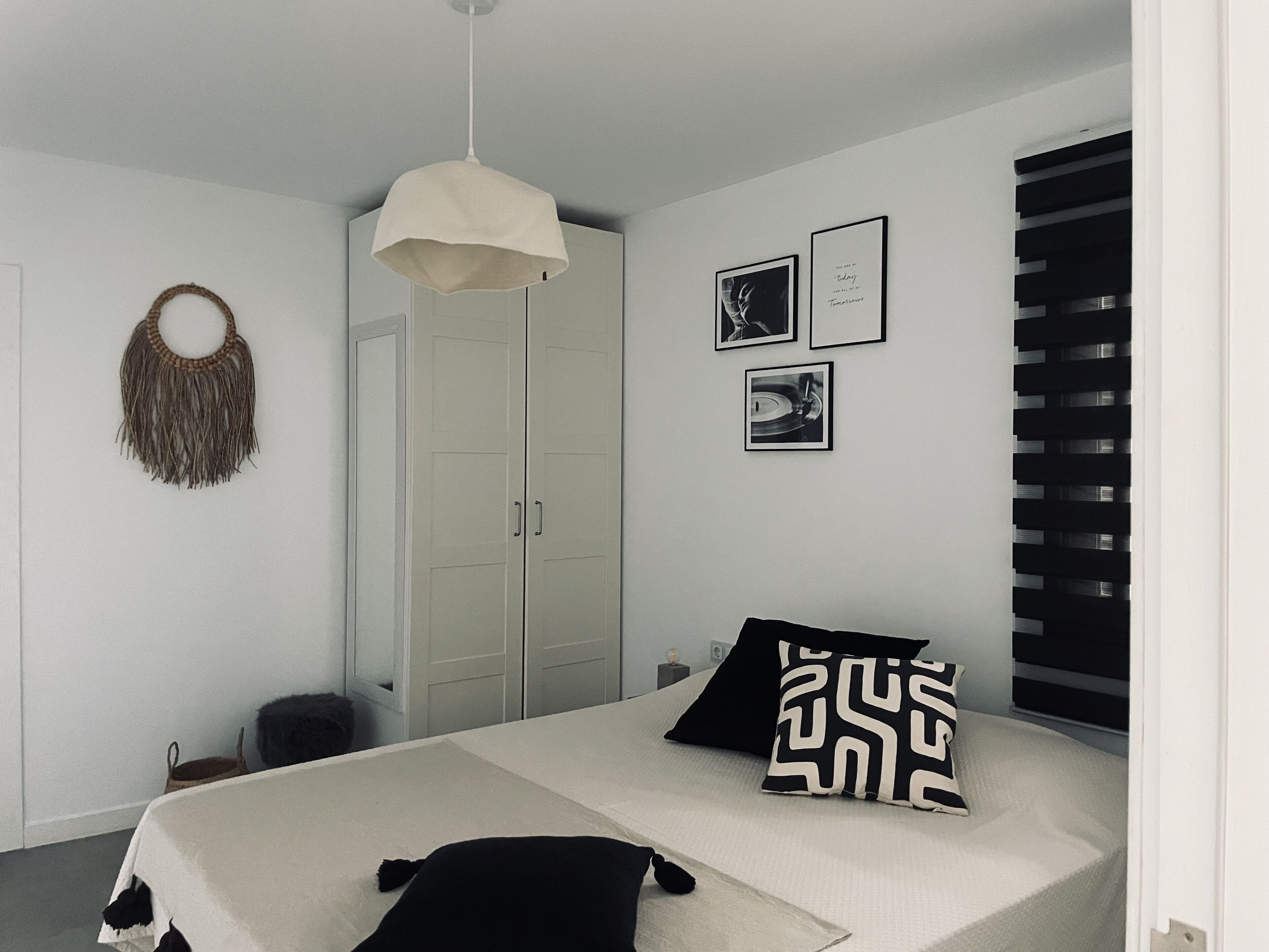 Een slaapkamer met een bed, een hanglamp, een kledingkast en een aan de muur bevestigd fotolijstje.