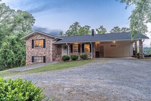 A single-story brick house with a covered front porch, a garage, and a gravel driveway.