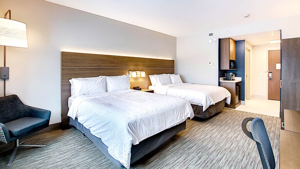 Une chambre d’hôtel avec deux lits, un bureau, une chaise et une salle de bain visible à travers une porte ouverte.
