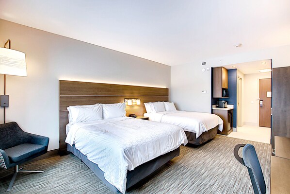 Une chambre d’hôtel avec deux lits, un bureau, une chaise et une salle de bain visible à travers une porte ouverte.
