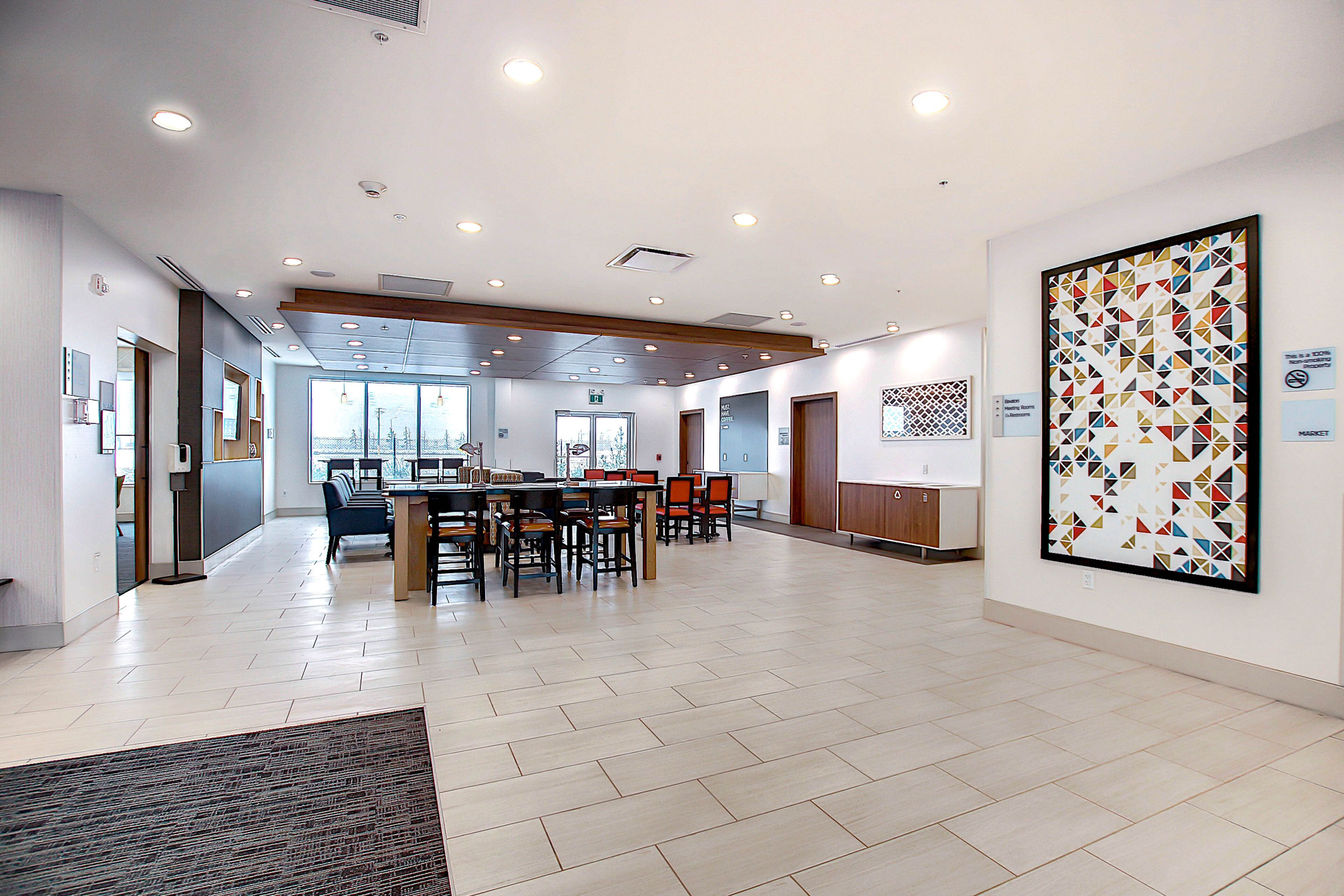 A spacious lobby with a long reception desk, multiple seating areas, and a large abstract art piece on the wall.