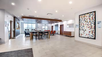 A spacious lobby with a long reception desk, multiple seating areas, and a large abstract art piece on the wall.