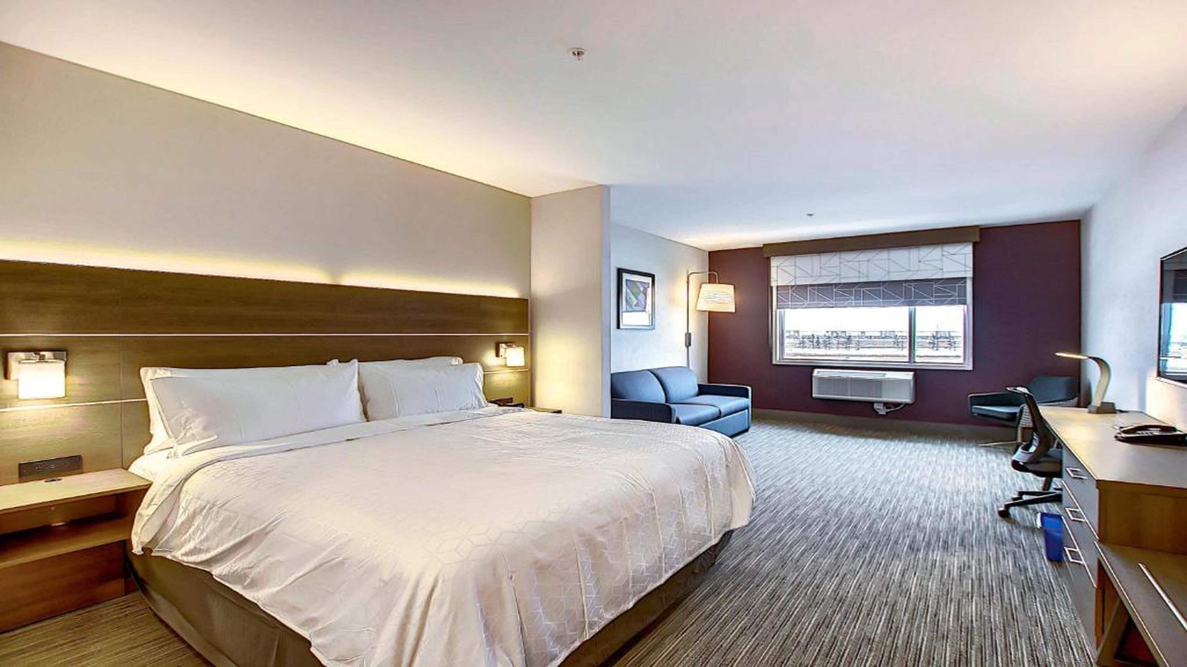 A hotel room with a large bed, a desk, a chair, and a window with a view.