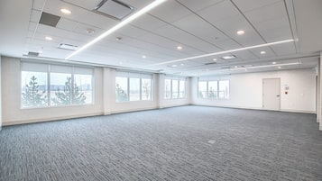 A large, empty conference room with carpeted flooring, large windows, and a door.