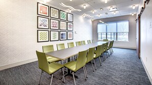 A conference room with a long table and chairs, framed artwork on the wall, and a large window.