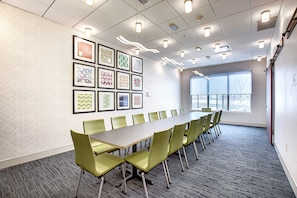 Une salle de conférence avec une longue table et des chaises, des œuvres d’art encadrées au mur et une grande fenêtre.