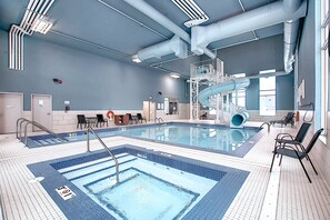 An indoor swimming pool with a central water slide, multiple lanes, and a lifeguard station. - Holiday Inn Express & Suites Calgary Airport Trail NE by IHG (Calgary)