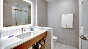 Une salle de bain moderne avec un grand miroir, un lavabo blanc et une cabine de douche en verre.